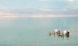 Zwei Frauen entspannen sich lesend im Toten Meer, dessen hoher Salzgehalt sie mühelos trägt. Der Meeresspiegel ist ruhig.