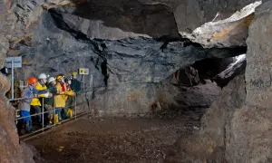 Besucher erkunden eine Höhle im Erzgebirge. Sie tragen Schutzhelme und blicken in die Tiefe des Bergwerks.