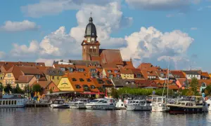 Hafen mit vielen Booten und einem Restaurant, hinter dem sich eine Stadt mit Kirchturm und roten Dächern erstreckt. Perfekte ausflugsziele waren.