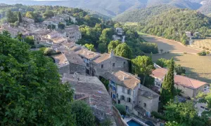 Dächer und Steinhäuser eines Dorfes im Luberon, Provence, eingebettet in grüne Hügel und Felder.