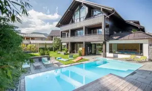 Moderner Poolbereich mit Liegestühlen und Blick auf ein stilvolles Holzhaus. Hier finden Sie die besten Oberstdorf Geheimtipps für Ihren Urlaub.