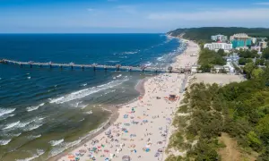 Blick auf die belebte Misdroy Promenade mit Strand, Meer und Seebrücke. Viele Menschen genießen den sonnigen Tag am Ostseestrand.