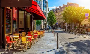 Ein sonniger Tag in Oberkampf, Paris. Rote und gelbe Stühle laden vor einem Café zum Verweilen ein.