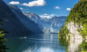 Ein Boot fährt auf einem ruhigen See, umgeben von steilen, bewaldeten Bergen. Ein idyllisches Bild von Badeseen Deutschland.