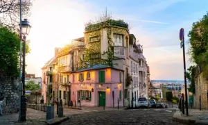 Malerische Gasse in Paris, perfekt für Sightseeing. Ein rosa Restaurant mit grünen Fensterläden und ein Mann mit Maske auf dem Kopfsteinpflaster.