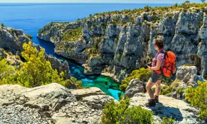 Frau mit Rucksack genießt den Ausblick beim Marseille Wandern. Türkisblaues Wasser in einer Felsbucht.