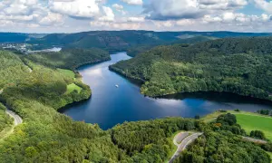 Idyllische Seenlandschaft in der Eifel mit kurviger Straße und einem Schiff. Entdecken Sie diese Eifel Geheimtipps!