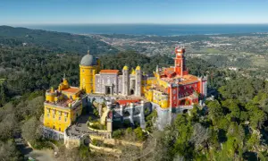 Buntes Schloss Pena thront auf Hügel, mit Blick auf das Meer. Ein grünes Auto parkt am sintra parking Weg.