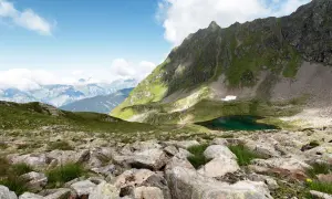 Bergsee bei Schruns, ideal zum Wandern. Grüne Hänge, Felsen und ein tiefblauer Bergsee unter blauem Himmel.