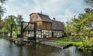 Historische Wassermühle am Wasser, perfekt für einen Spreewald Tagesausflug. Ein idyllischer Ort mit viel Grün und Wasser.