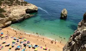 Sonniger Strand an der Algarve, ein echter Geheimtipp mit türkisfarbenem Wasser, Felsen und vielen bunten Sonnenschirmen.