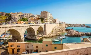 Bogenbrücke über einem Hafen mit Booten und Häusern, die sich an einen Hügel schmiegen. Die malerische marseille altstadt erstreckt sich bis zum türkisfarbenen Meer.
