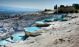 Travertinterrassen von Pamukkale heute: Türkisblaue Pools auf weißen Kalksteinterrassen, mit Besuchern im Hintergrund und antiken Ruinen.