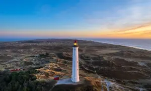 Leuchtturm bei Sonnenuntergang an der Küste, umgeben von Dünen. Ein versteckter Ort, der an Hvide Sande Geheimtipps erinnert.
