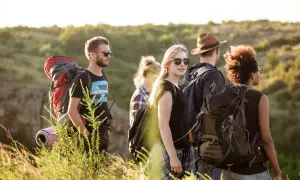 Eine Gruppe junger Leute lernt wandern. Sie tragen Rucksäcke und genießen die Natur bei Sonnenschein.
