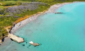 Traumhafter Strand in Apulien mit türkisfarbenem Wasser, sonnenhungrigen Menschen und grünen Hügeln im Hintergrund.