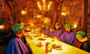 Festlich gedeckter Tisch im Bergwerk Annaberg. Gäste in Schutzhelmen und Umhängen speisen bei Kerzenlicht in der Felsenkammer.