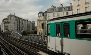 Ein Pariser Métro-Zug fährt auf den Gleisen in Richtung Saint-Lazare. Gebäude und eine Brücke säumen die Strecke.