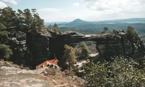 Felsentor in Böhmischer Schweiz, nahe dem Erzgebirge Tschechien. Ein malerischer Ausblick auf bewaldete Hügel und eine kleine Hütte.