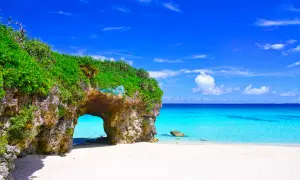Traumhafter Strand mit Felsentor auf der Okinawa Insel. Türkises Meer und weißer Sand unter blauem Himmel.