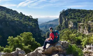 Wanderer mit Rucksack auf Felsen sitzend, genießt die Aussicht auf ein tiefes Tal auf dem Mallorca Fernwanderweg.