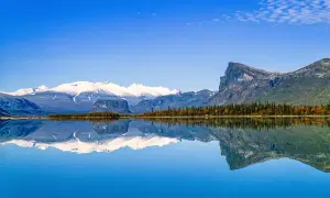 Spiegelglatte Wasserfläche reflektiert schneebedeckte Berge und herbstliche Bäume in einem schwedischen Nationalpark.