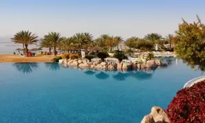Ein Infinity-Pool mit Blick auf das jordanische Meer, Palmen und einen Sandstrand.