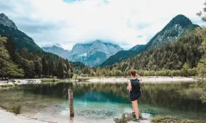 Frau mit Rucksack genießt den Ausblick auf den Jasna See und die Berge. Perfekt für Kranjska Gora Wandern.