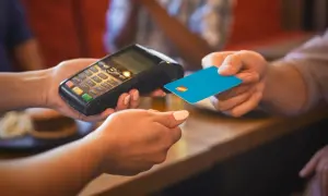 Eine Person bezahlt mit einer blauen Karte an einem Terminal. Das ist eine typische Transaktion, wenn man in Frankreich Geld ausgibt.