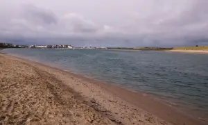 Sandiger Strand mit Blick auf eine Stadt und einen Yachthafen. Der Himmel ist bewölkt, aber das Wasser am Emden Strand ist ruhig.