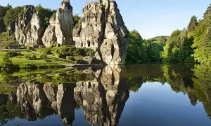 Felsformationen mit kleinen Höhlen spiegeln sich in einem ruhigen See. Ein idyllischer Ort für eine Wanderung im Teutoburger Wald.