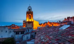 Aix-en-Provence Geheimtipps: Ein beleuchteter Kirchturm ragt über die Dächer der Altstadt im Abendlicht.