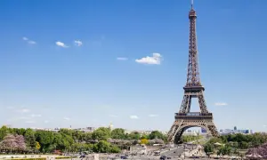 Eiffelturm, ein Paris must see, ragt in den blauen Himmel. Menschen genießen den sonnigen Tag im Park.