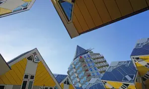 Rotterdam Geheimtipps: Schräge Würfelhäuser und ein futuristisches Hochhaus unter blauem Himmel.