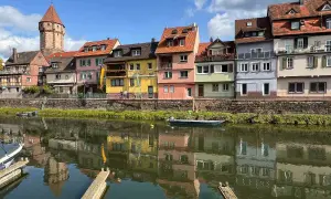Bunte Häuserfront am Flussufer, ein Turm ragt empor. Hier könnte das Taubertal sein, mit Spiegelungen im Wasser.