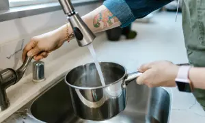 Eine Hand dreht den Wasserhahn auf, um einen Topf mit Leitungswasser aus Budapest zu füllen.
