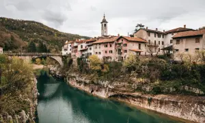 Idyllisches Dorf am Fluss Soča in Slowenien, mit einer Brücke und traditionellen Häusern, die sich an den Hang schmiegen.