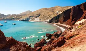 Der Rote Strand von Santorini mit türkisfarbenem Wasser, Segelbooten und Menschen, die sich auf dem roten Sand entspannen.
