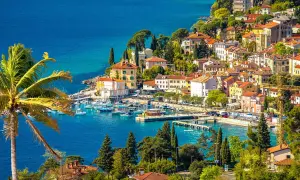 Bunte Häuser am Meer, Boote im Hafen und eine Palme – ein malerischer Blick auf Opatija, der Lust auf Entdeckungen macht. Hier gibt es viele Opatija Geheimtipps zu entdecken.