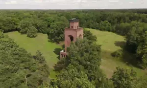 Ein roter Backsteinturm ragt aus einer grünen Wiese im Spreewald, umgeben von üppigen Bäumen.