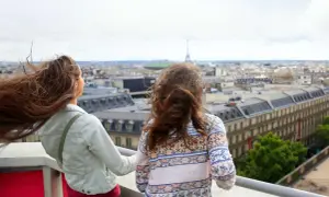 Zwei Teenager genießen den Blick über Paris. Der Wind spielt mit ihren Haaren, während sie die Stadt und den Eiffelturm bestaunen.