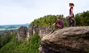 Zwei Kletterer auf den Affensteinen genießen die Aussicht. Ein Mann sitzt, eine Frau steht. Kein Hund zu sehen.