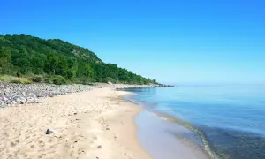 Sandstrand mit Felsen und grünen Hügeln, ein Highlight der schwedischen Landschaft.