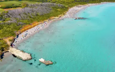 Traumhafter Strand in Apulien mit türkisfarbenem Wasser, sonnenhungrigen Menschen und grünen Hügeln im Hintergrund.