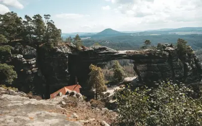 Felsentor in Böhmischer Schweiz, nahe dem Erzgebirge Tschechien. Ein malerischer Ausblick auf bewaldete Hügel und eine kleine Hütte.