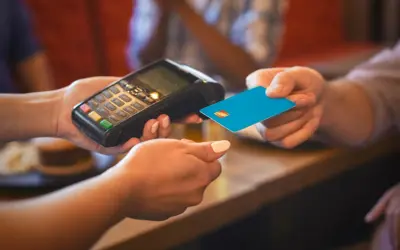 Eine Person bezahlt mit einer blauen Karte an einem Terminal. Das ist eine typische Transaktion, wenn man in Frankreich Geld ausgibt.