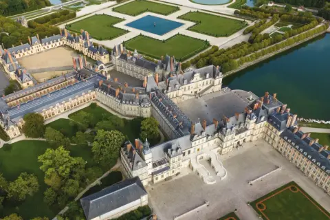 Luftaufnahme des prächtigen Schlosses Fontainebleau mit seinen weitläufigen Höfen, Gärten und einem See.
