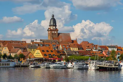Hafen mit vielen Booten und einem Restaurant, hinter dem sich eine Stadt mit Kirchturm und roten Dächern erstreckt. Perfekte ausflugsziele waren.