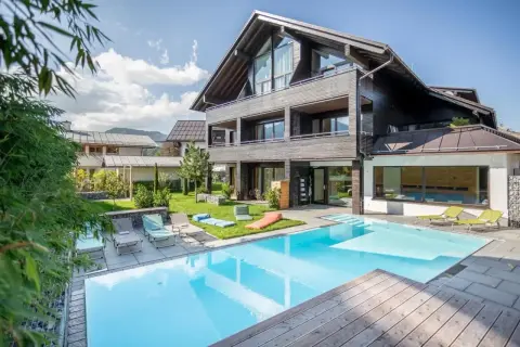 Moderner Poolbereich mit Liegestühlen und Blick auf ein stilvolles Holzhaus. Hier finden Sie die besten Oberstdorf Geheimtipps für Ihren Urlaub.
