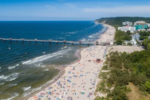 Blick auf die belebte Misdroy Promenade mit Strand, Meer und Seebrücke. Viele Menschen genießen den sonnigen Tag am Ostseestrand.